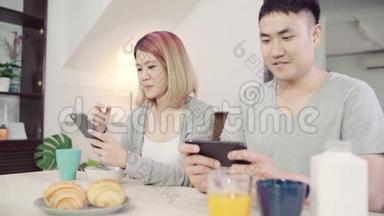 漂亮的亚洲年轻夫妇在吃早餐时，一边拿着报纸和手机，一边在桌子上分心。